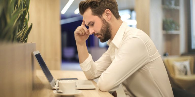 hand on forehead of a man looking at a laptop