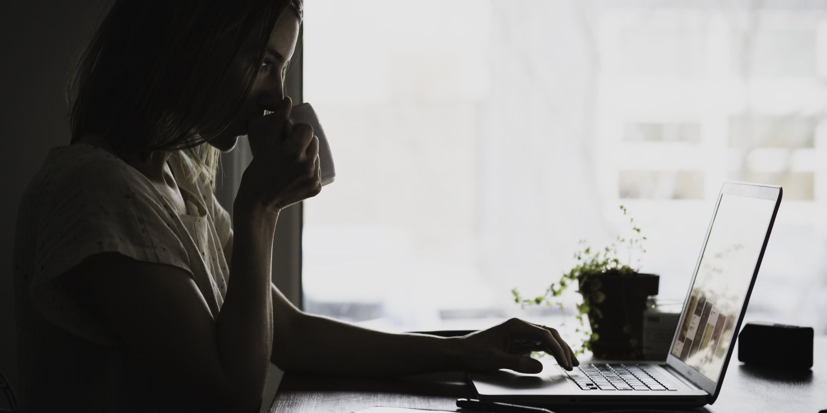 a girl sips a beverage while working on her laptop