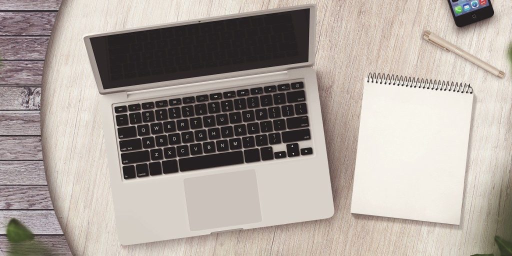 A silver laptops with a notepad on a wooden table.jpg