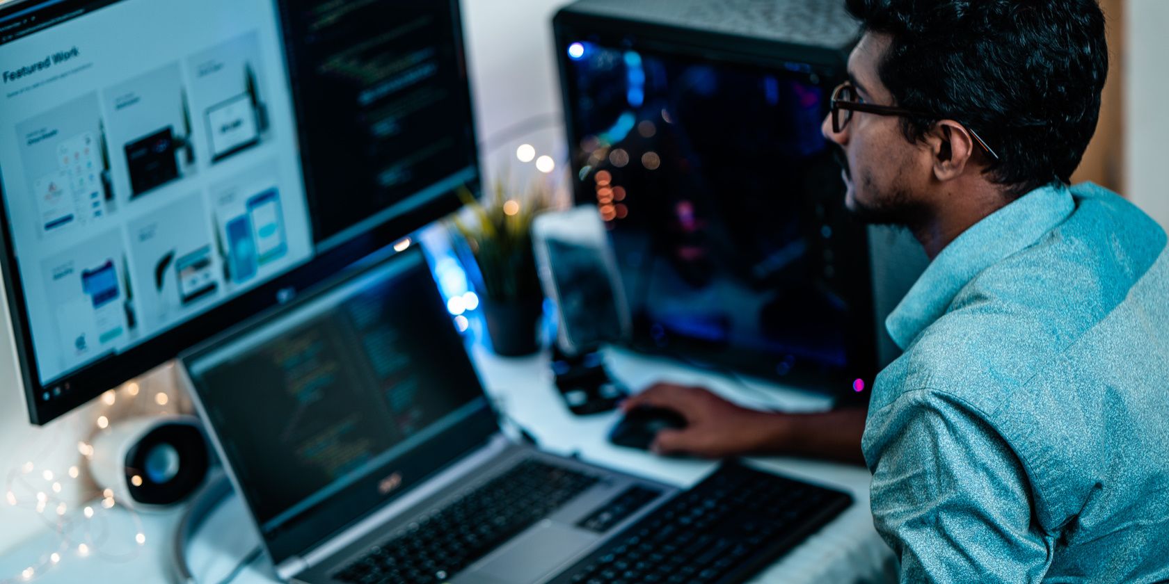 a man uses his laptop and a desktop computer for work