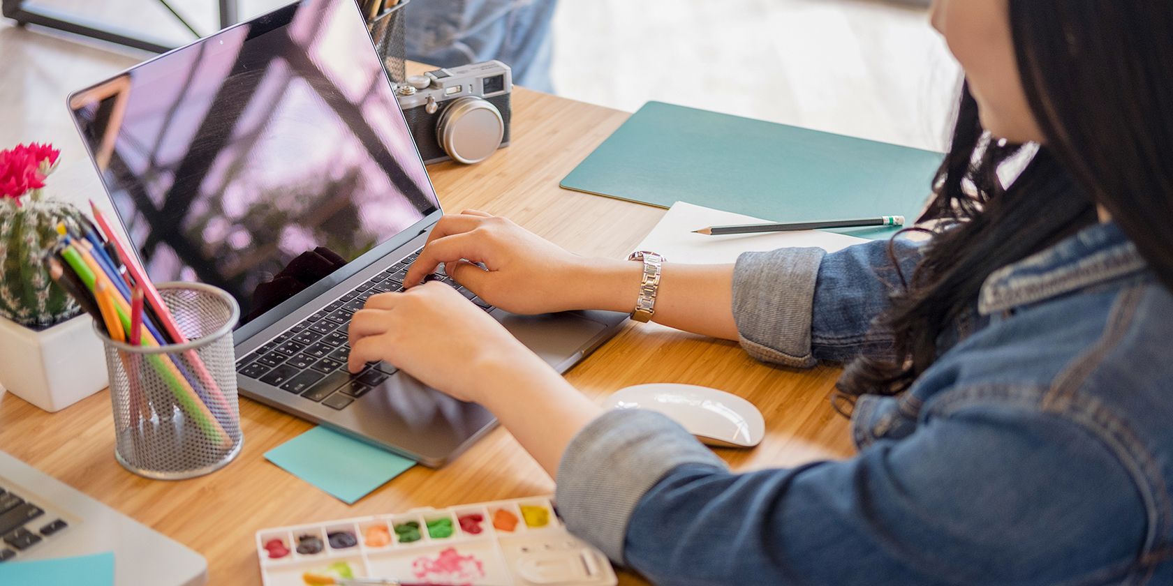 Woman Using Laptop With Art Supplies And Camera On Table.jpg